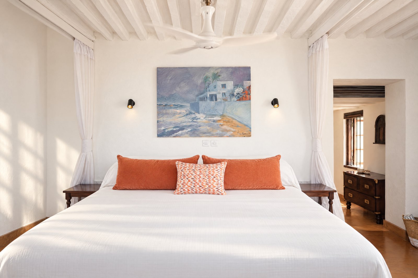 Orange-cushion double bedroom beneath coastal painting